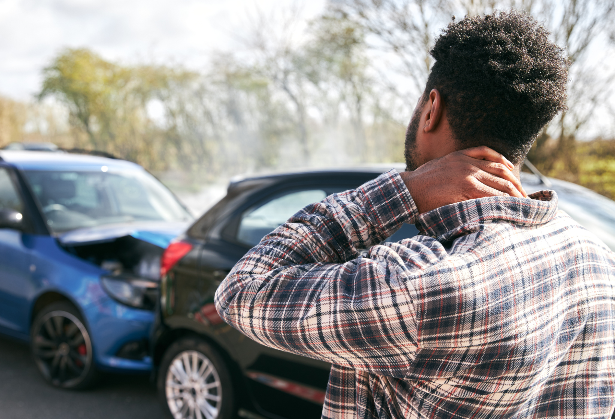 Man seen from behind, hands on neck, standing in a parking lot with blue cars in the background. car accident comparative negligence | Gabrielson Law Offices, LTD car accident comparative negligence | Gabrielson Law Offices, LTD