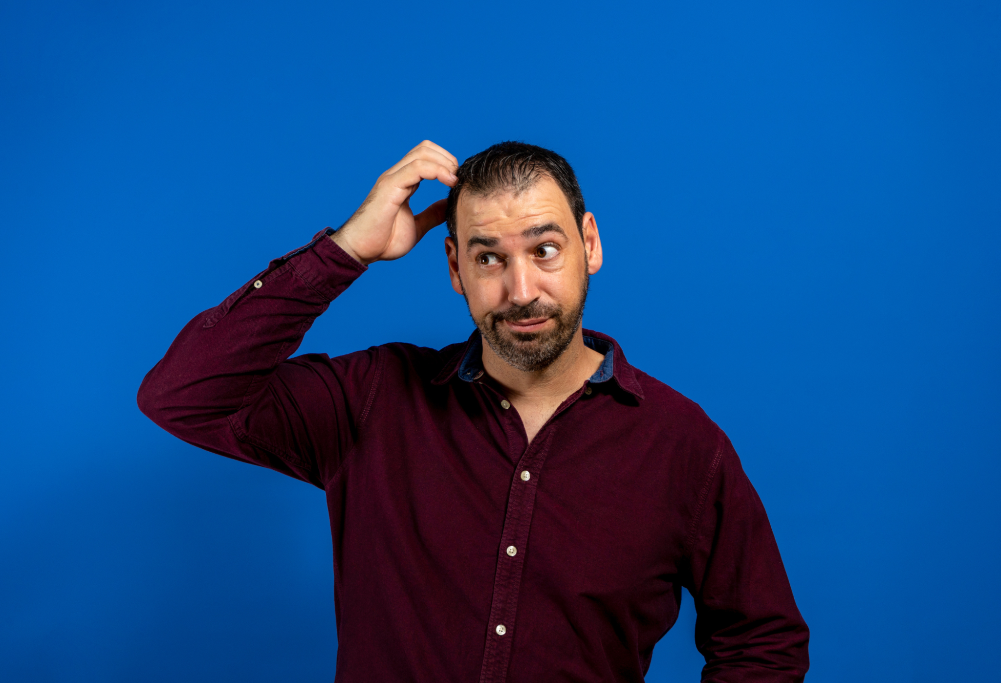 Man in a burgundy shirt scratching his head against a solid blue background. how much is my claim worth | Gabrielson Law Offices, LTD how much is my claim worth | Gabrielson Law Offices, LTD