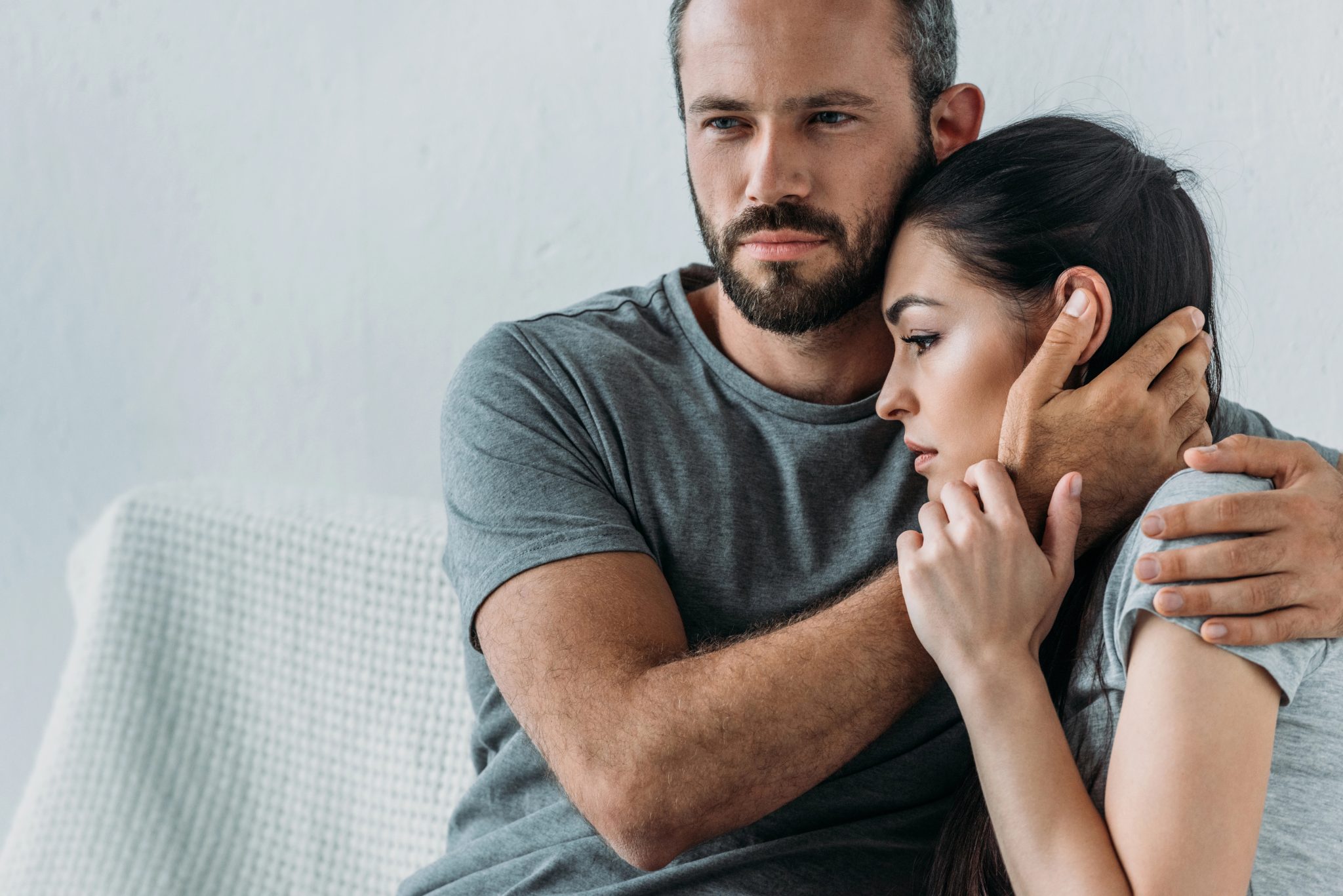 Couple cuddling on a gray sofa, the man holding the woman close with a protective arm around her shoulders. noneconomic personal injury damages brainerd MN | Gabrielson Law Offices, LTD noneconomic personal injury damages brainerd MN | Gabrielson Law Offices, LTD